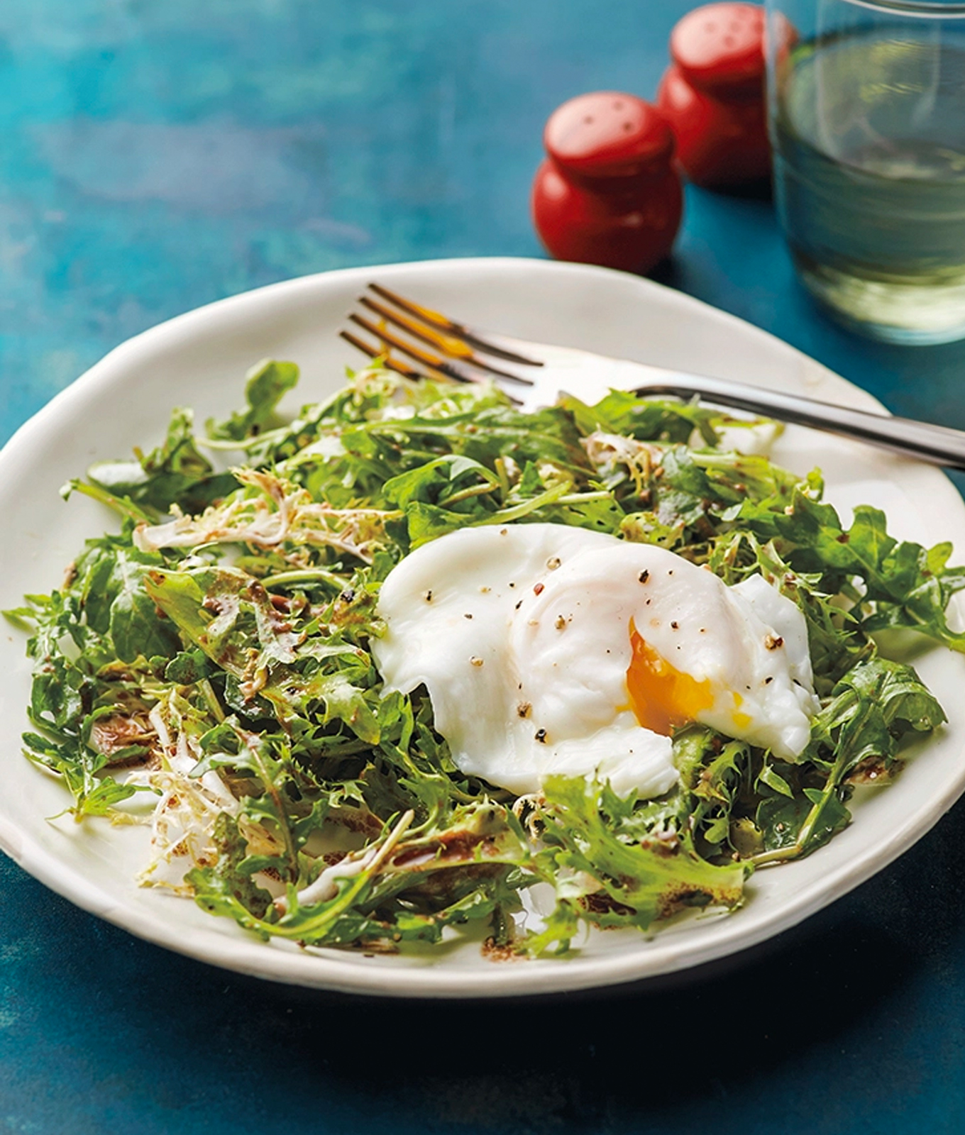 Brunch Recipes: Poached Egg with Frisée and Arugula Salad in rounded plate with red salt and pepper shakers in behind