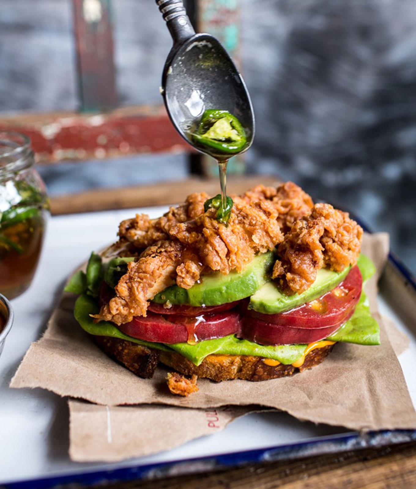 jalapeño recipes: fried chicken blt being drizzled with jalapeno honey