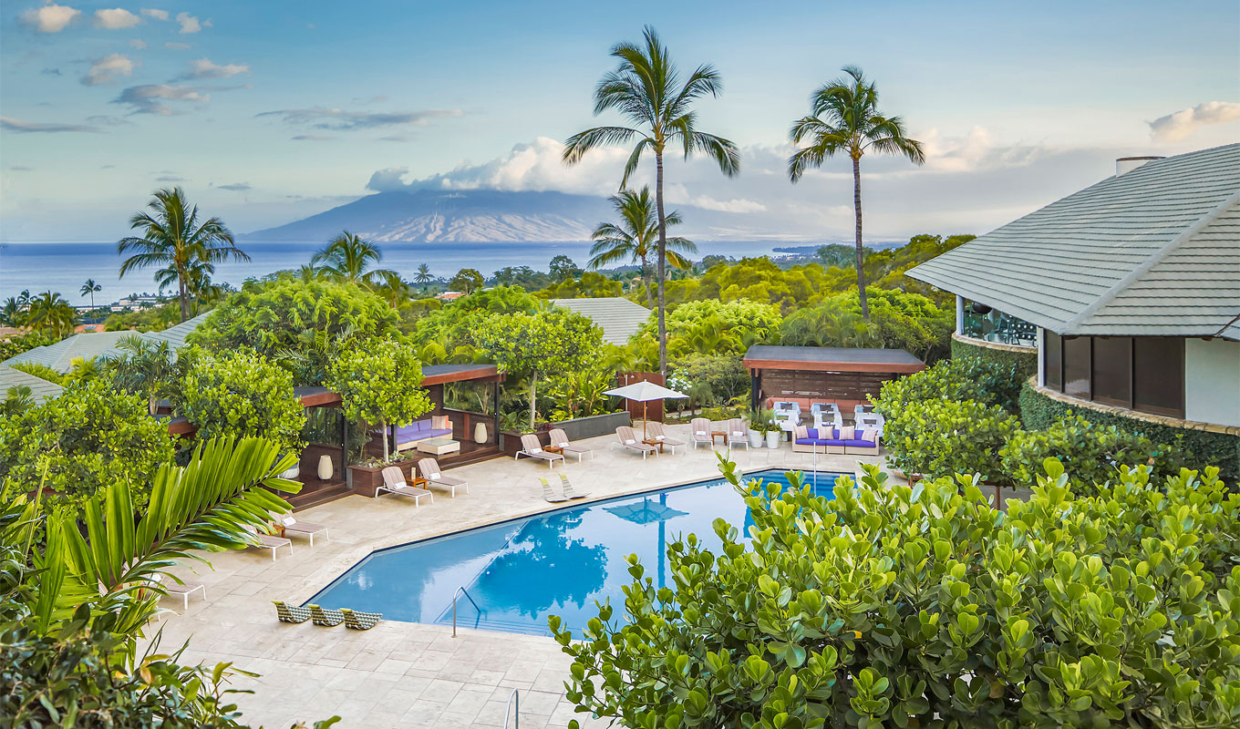 Best Hotels in Wailea Hawaii - An aerial view of the Hotel Wailea, Relais & Châteaux. It features a view of one of the property's buildings, a pool, palm trees, lounge chairs and views of the mountains in the distance.