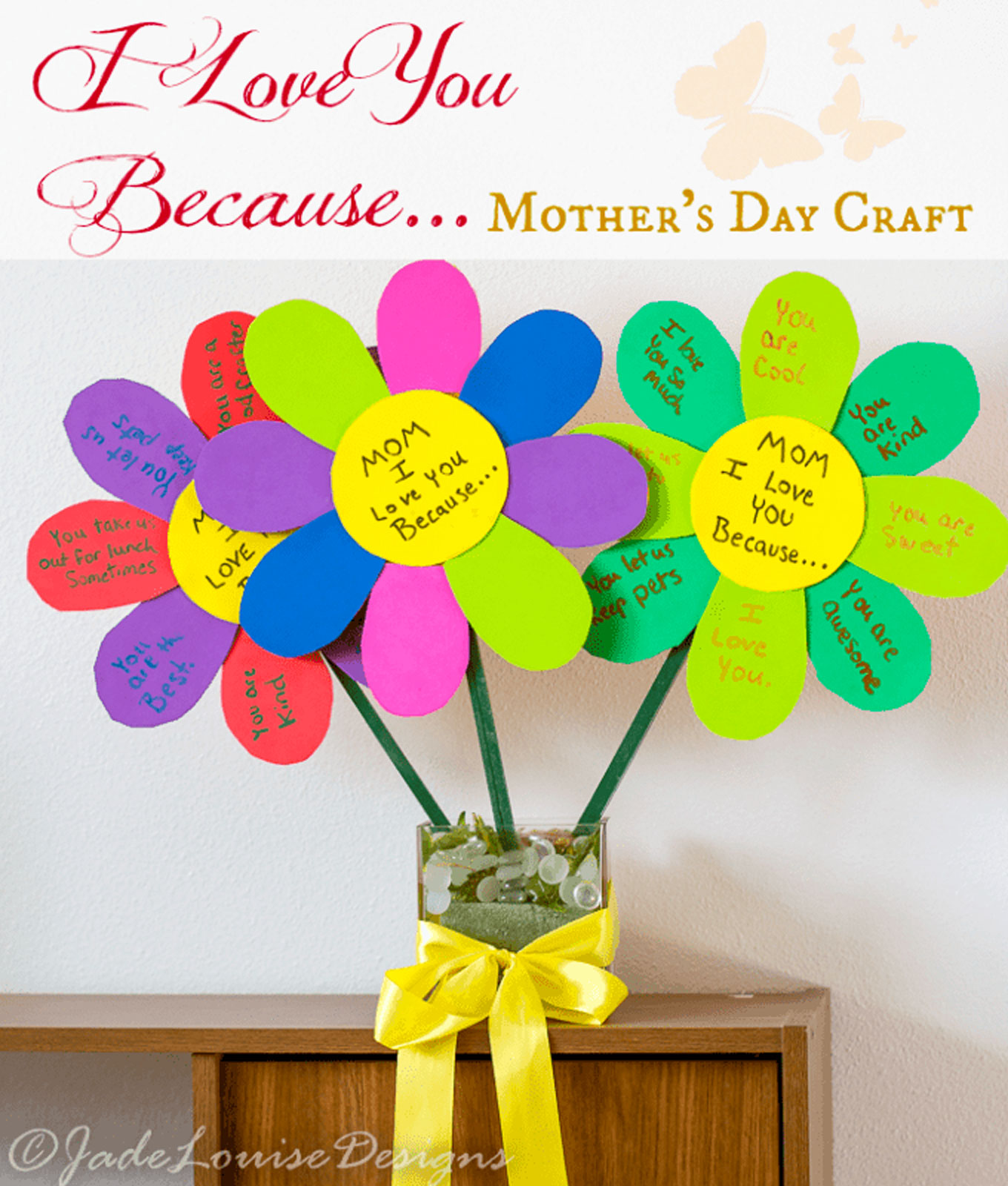 mothers-day-crafts: A papercraft made in the shape of flowers with handwritten notes on the petals. They are positioned in a glass vase on a wooden table.