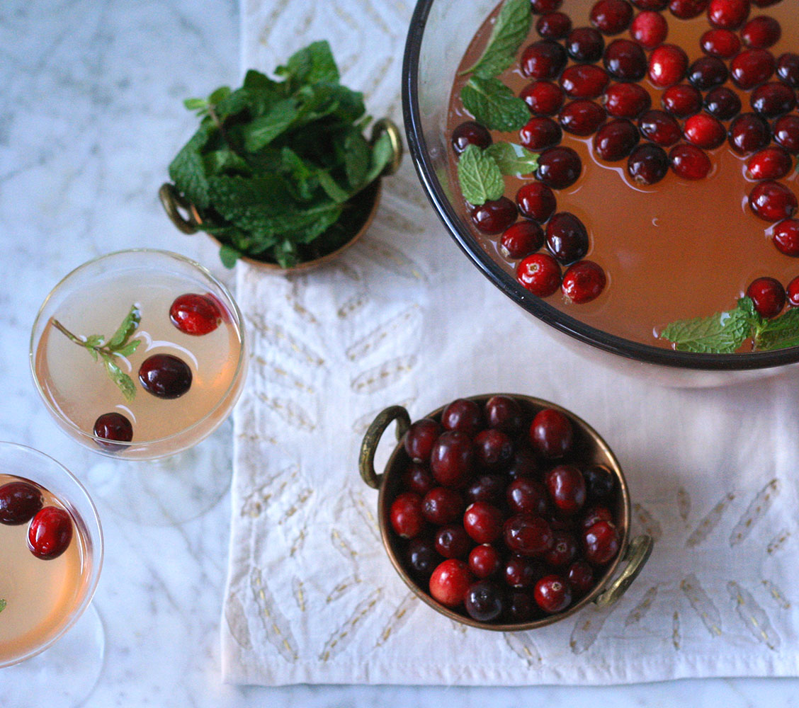 holiday punch bowl cocktails: cranberry mint cocktail in a bowl with two glasses and a bowl of cranberries