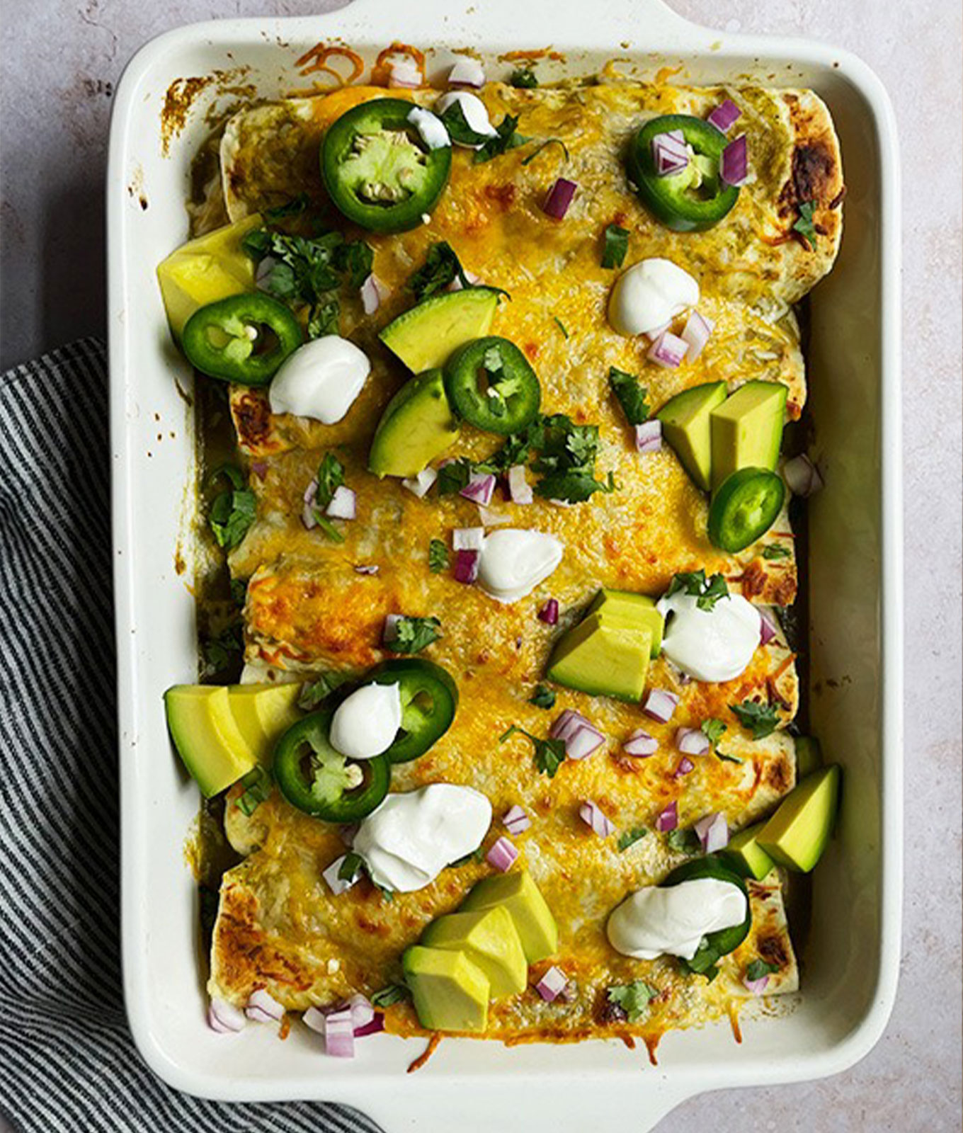 a dish of green-chicken-enchiladas topped with avocado, sour cream and jalapeños