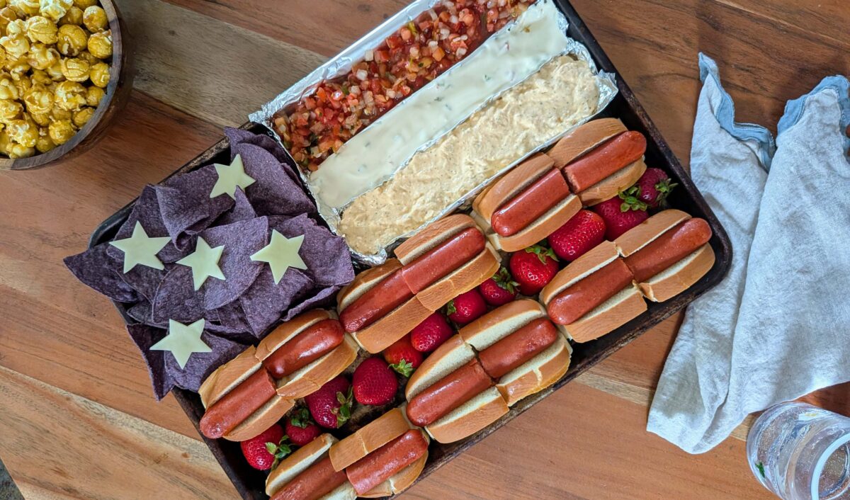 hot dogs in rows with strawberries, blue corn tortilla chips and various dips forming an American flag